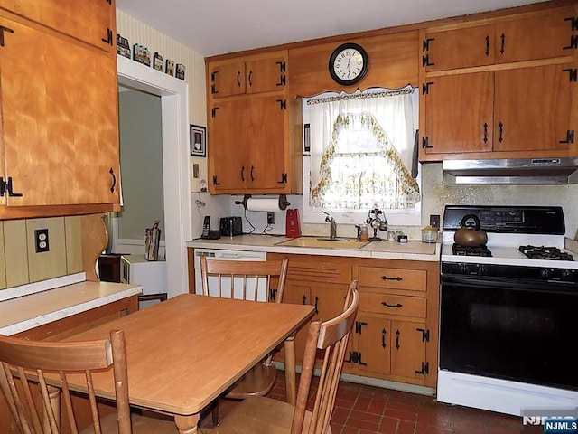 kitchen featuring under cabinet range hood, a sink, light countertops, brown cabinetry, and range with gas cooktop