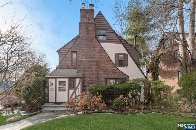 tudor house with a shingled roof, a chimney, a front lawn, and stucco siding