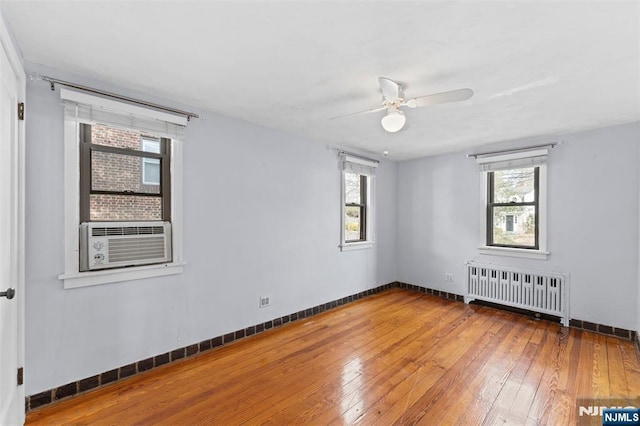 empty room with cooling unit, wood-type flooring, baseboards, and radiator heating unit