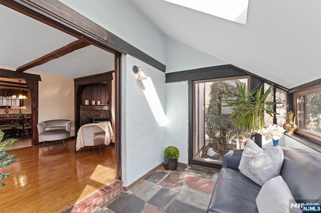 interior space with a skylight, a brick fireplace, wood finished floors, and baseboards