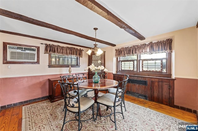 dining space with a wainscoted wall, an AC wall unit, beamed ceiling, and wood finished floors