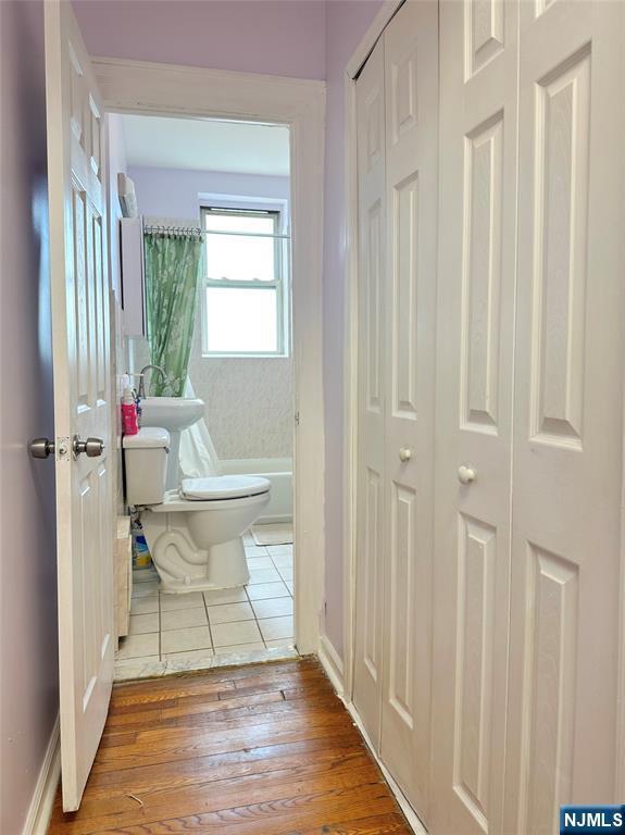 bathroom featuring a closet, wood-type flooring, a tub to relax in, and toilet