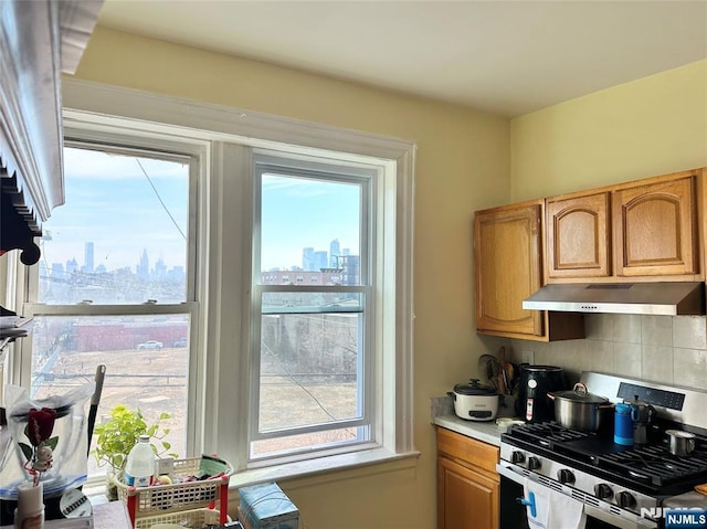 kitchen with under cabinet range hood, tasteful backsplash, a city view, and stainless steel range with gas stovetop