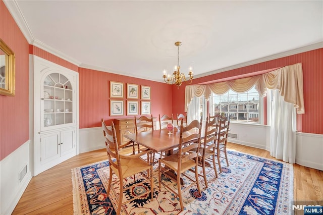 dining room with an inviting chandelier, visible vents, wood finished floors, and ornamental molding