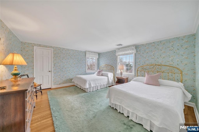 bedroom with wood finished floors, visible vents, baseboards, ornamental molding, and wallpapered walls