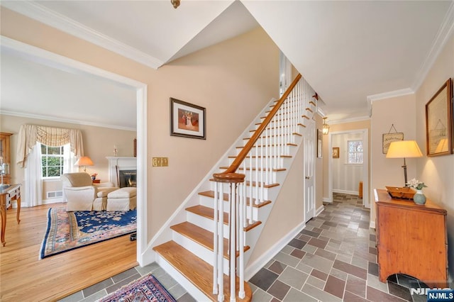 staircase featuring visible vents, baseboards, wood finished floors, a lit fireplace, and crown molding