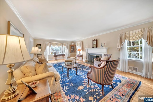 living area with light wood-style flooring, a fireplace with flush hearth, visible vents, baseboards, and crown molding