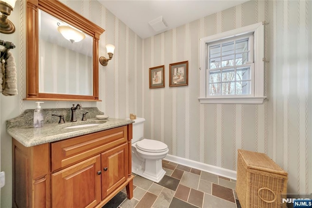 bathroom featuring visible vents, toilet, vanity, baseboards, and wallpapered walls