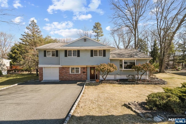 split level home with a front lawn, brick siding, driveway, and an attached garage