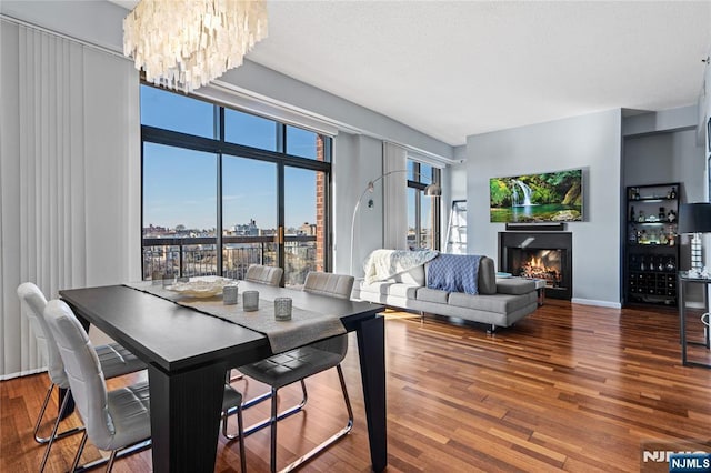 dining space featuring a warm lit fireplace, baseboards, wood finished floors, and a chandelier