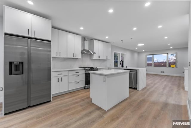 kitchen featuring wall chimney exhaust hood, appliances with stainless steel finishes, a center island, a peninsula, and light countertops