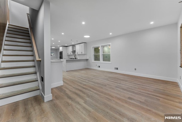 unfurnished living room featuring visible vents, light wood-style flooring, stairway, a sink, and recessed lighting