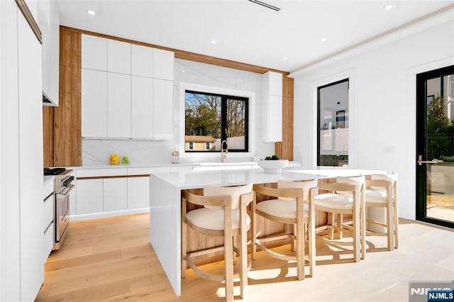 kitchen featuring a kitchen island, stainless steel stove, white cabinets, modern cabinets, and a sink