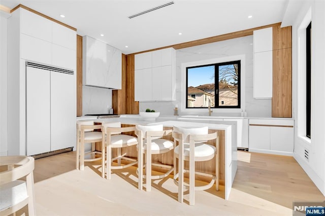 kitchen with paneled refrigerator, modern cabinets, a kitchen breakfast bar, a kitchen island, and white cabinetry