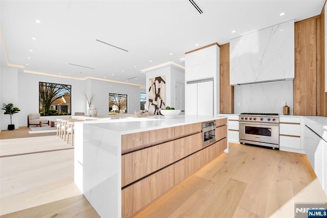 kitchen featuring premium range hood, light brown cabinetry, open floor plan, premium appliances, and modern cabinets