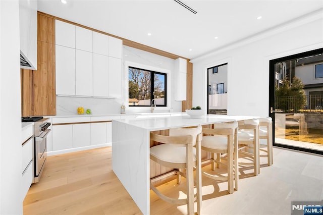 kitchen featuring a kitchen island, a breakfast bar, stainless steel range, white cabinets, and modern cabinets