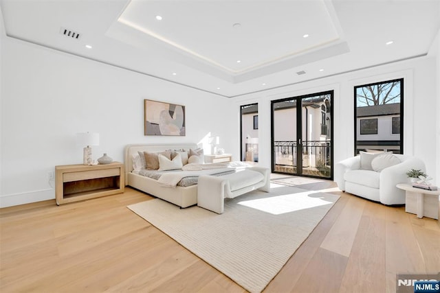 bedroom featuring a tray ceiling, light wood-style flooring, and access to outside