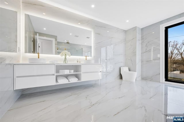 bathroom featuring toilet, double vanity, marble finish floor, stone wall, and a sink