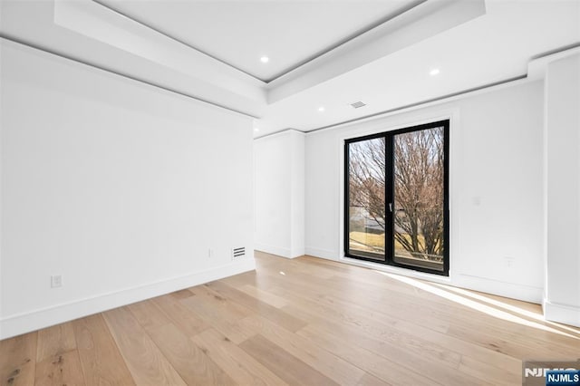 empty room with light wood-type flooring, a tray ceiling, baseboards, and visible vents