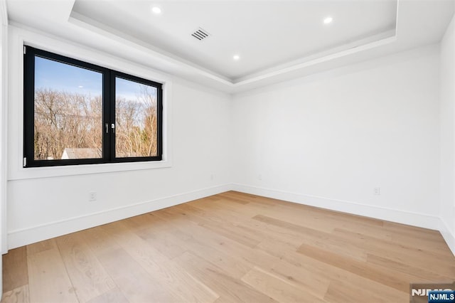 unfurnished room featuring visible vents, a raised ceiling, and light wood-style flooring