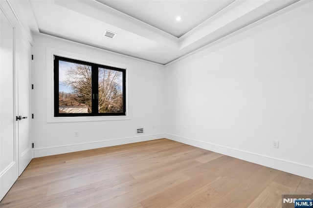 spare room with visible vents, a raised ceiling, light wood-style floors, and baseboards