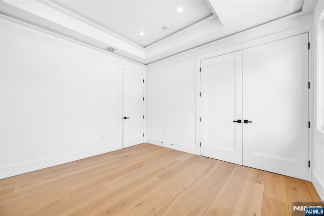 unfurnished bedroom featuring light wood finished floors, visible vents, baseboards, recessed lighting, and a raised ceiling