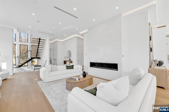 living area with a high end fireplace, stairway, recessed lighting, and light wood-style floors