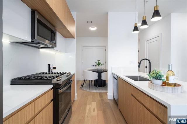 kitchen with a sink, stainless steel appliances, hanging light fixtures, and light countertops