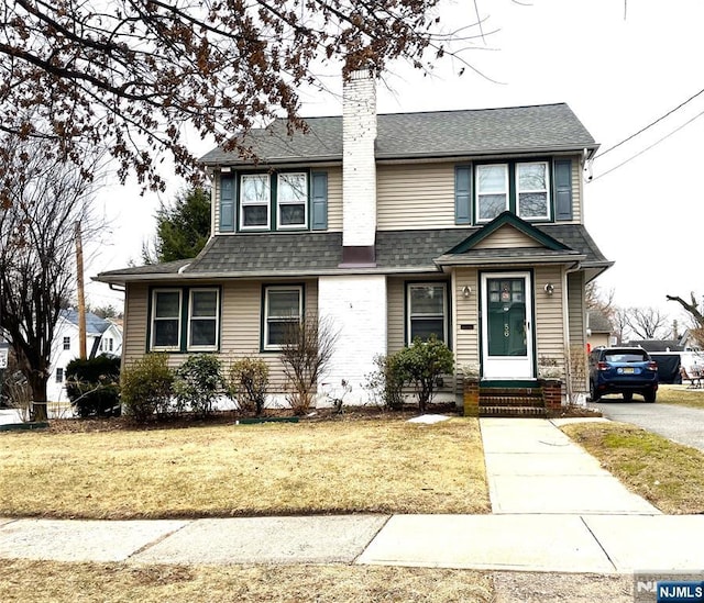 view of front of property featuring a shingled roof, a chimney, and a front yard