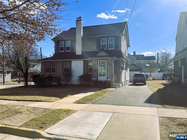 traditional home featuring driveway, a front lawn, a chimney, and fence