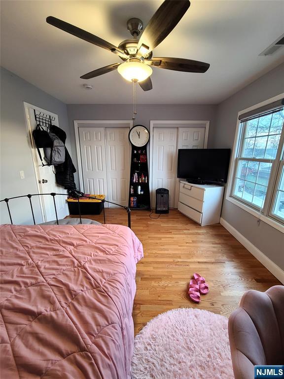 bedroom with baseboards, visible vents, a ceiling fan, light wood-type flooring, and multiple closets