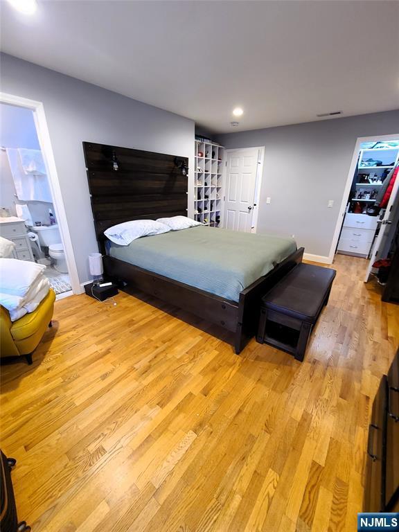 bedroom featuring light wood finished floors, baseboards, ensuite bathroom, a closet, and recessed lighting