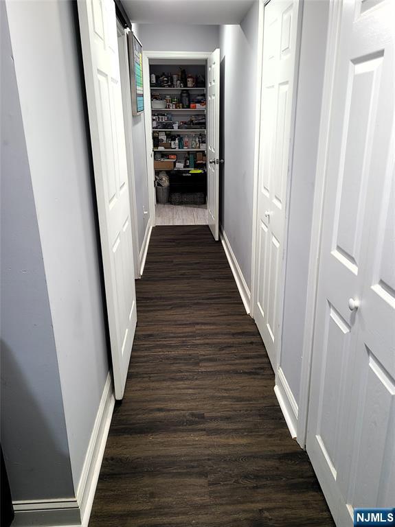 corridor with dark wood-type flooring and baseboards