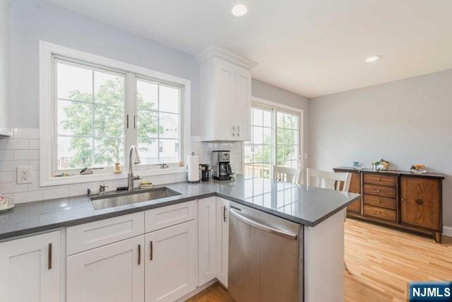 kitchen with white cabinets, a peninsula, stainless steel dishwasher, light wood-style floors, and a sink