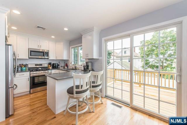 kitchen with visible vents, dark countertops, appliances with stainless steel finishes, a peninsula, and white cabinetry