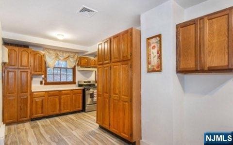 kitchen with light wood-style flooring, visible vents, electric stove, light countertops, and brown cabinets