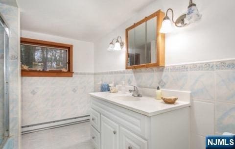 full bathroom with a baseboard heating unit, tile walls, a wainscoted wall, and vanity