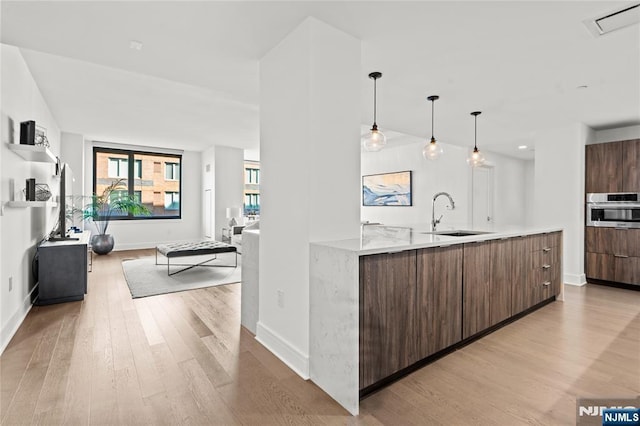 kitchen with light countertops, stainless steel oven, a sink, modern cabinets, and light wood-type flooring