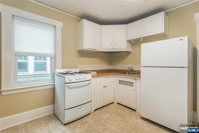 kitchen with white appliances, baseboards, white cabinets, a textured ceiling, and a sink