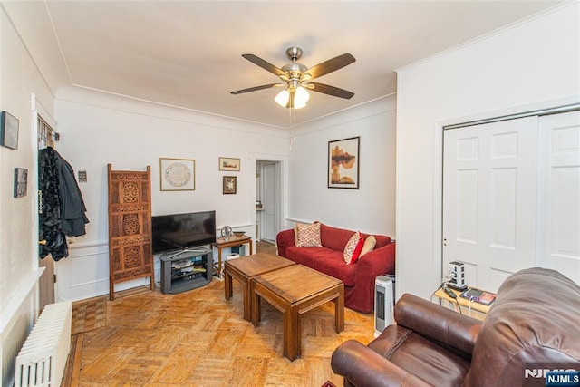 living room with a ceiling fan, crown molding, a decorative wall, and radiator heating unit