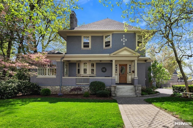 traditional style home featuring covered porch, a chimney, roof with shingles, and a front lawn