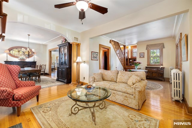 living room with crown molding, stairway, light wood-type flooring, arched walkways, and ceiling fan with notable chandelier