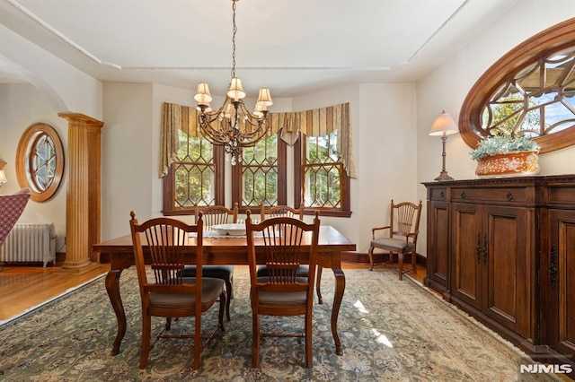 dining room with a healthy amount of sunlight, radiator, wood finished floors, and a notable chandelier