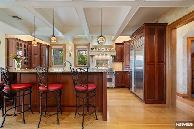 kitchen with visible vents, light wood-style floors, a kitchen breakfast bar, high quality appliances, and coffered ceiling