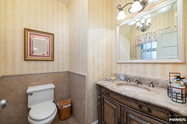 bathroom with wainscoting, vanity, toilet, a chandelier, and wallpapered walls
