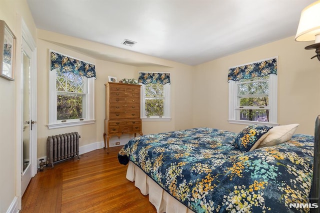 bedroom featuring visible vents, radiator heating unit, multiple windows, and wood finished floors