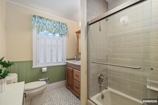 full bath with tile patterned flooring, wainscoting, vanity, combined bath / shower with glass door, and toilet