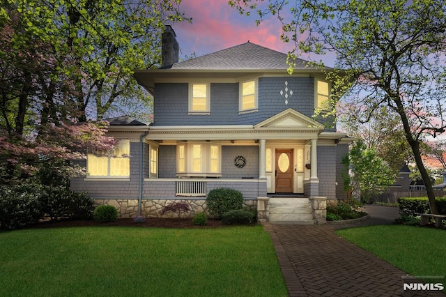 traditional style home featuring a porch, a chimney, a shingled roof, and a front yard
