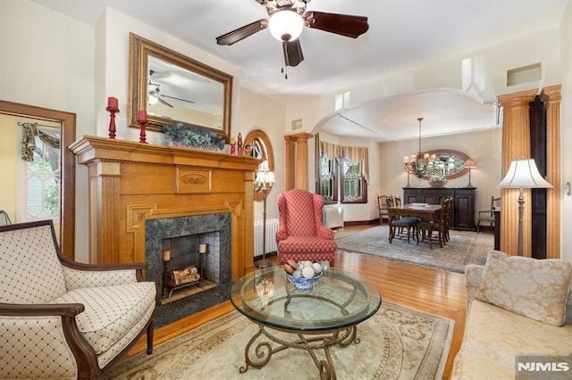sitting room featuring visible vents, wood finished floors, ceiling fan with notable chandelier, radiator heating unit, and a premium fireplace