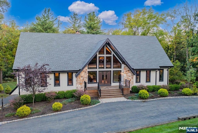 view of front of property featuring stone siding, a shingled roof, a chimney, and a porch